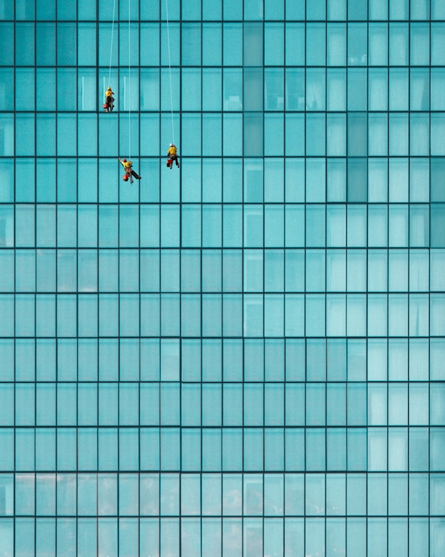 Example outsourcing solutions, image of window cleaners on ropes on side of glass building